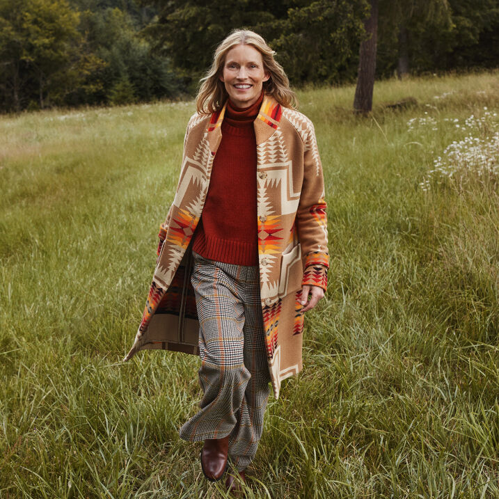 Woman walking through a field wearing a long Archive Blanket Coat