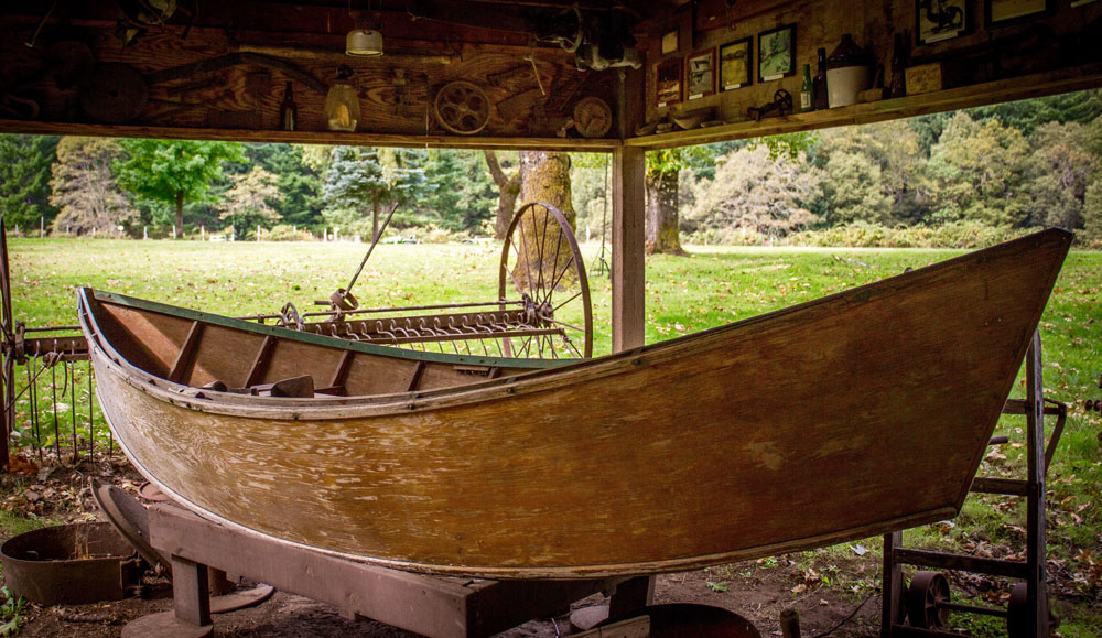 A wooden drift boat, part of a historical display, up on blocks in a shelter.