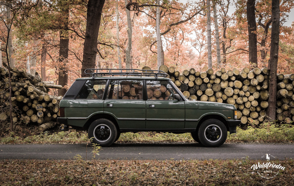 A vintage Range Rover parked by a woodpile