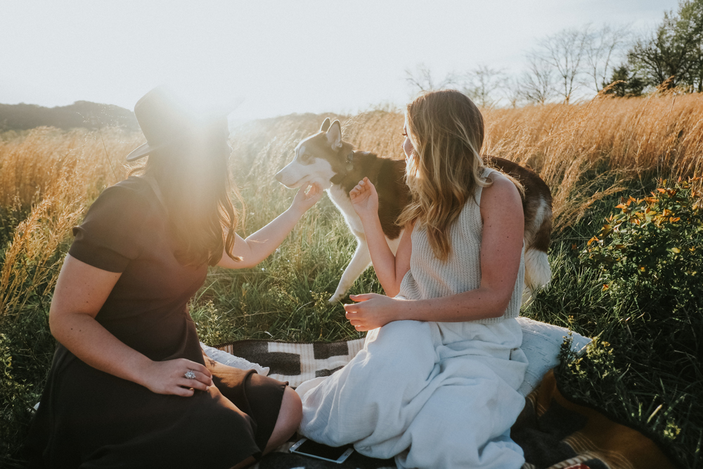 Two women pet a dog in a meadow.