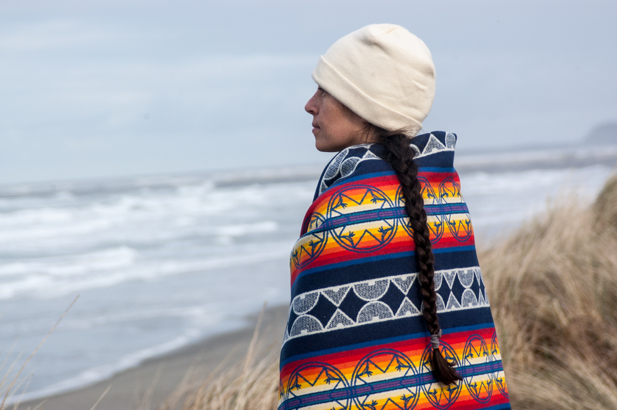 A woman shows off the We Walk Together blanket at Fort Stevens beach.