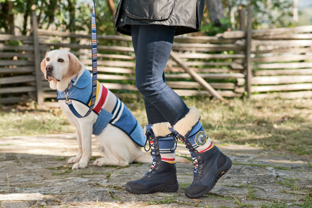 A Yellow Lab in a Pendleton dog coat, walked by a woman wearing Pendleton UGG boots.