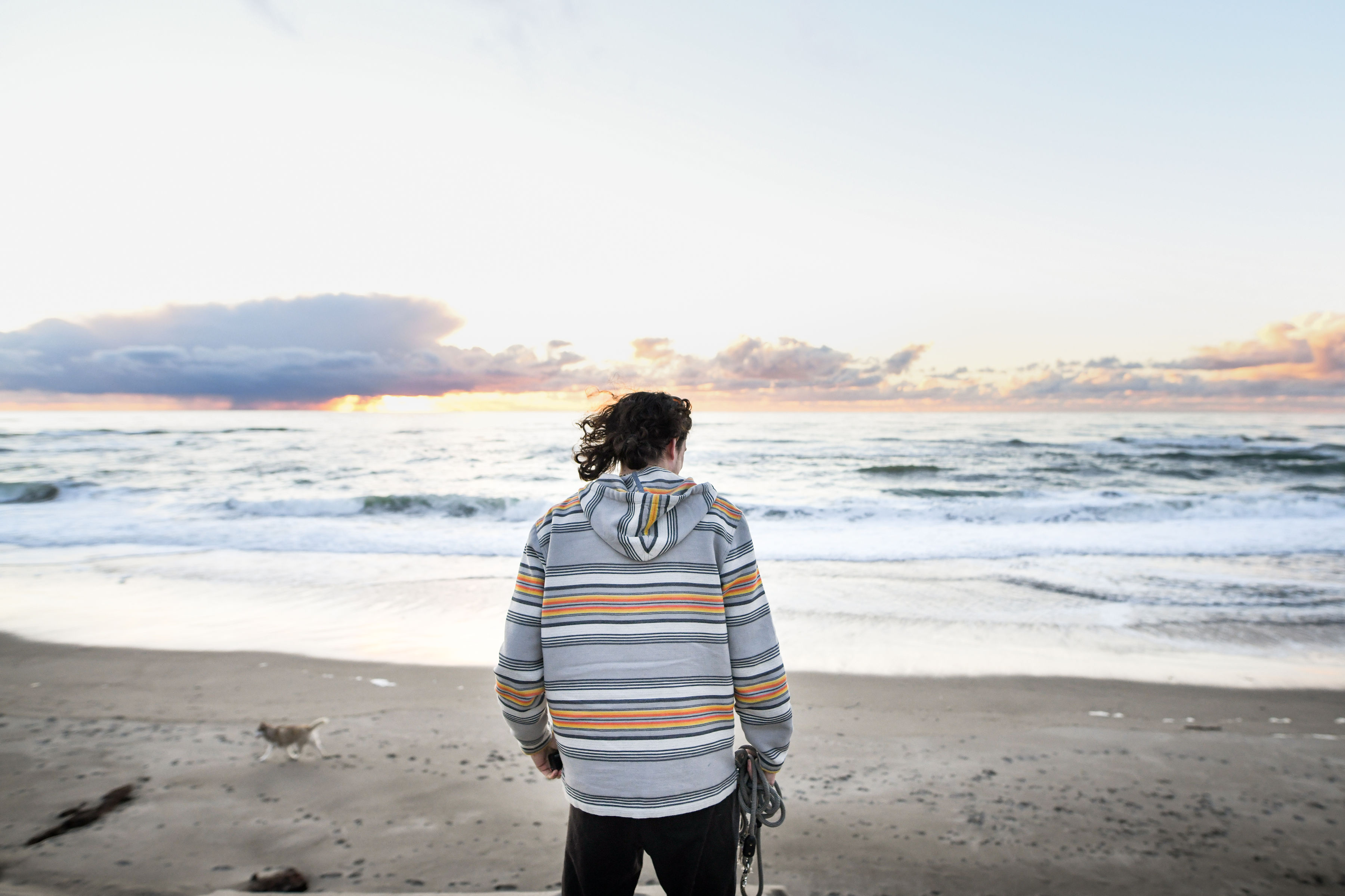 Man standing on beach wearing striped overshirt.