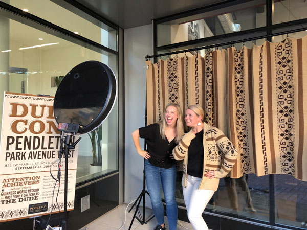 Two beautiful blond women pose in front of a Westerley blanket at DudeCon's photo booth.