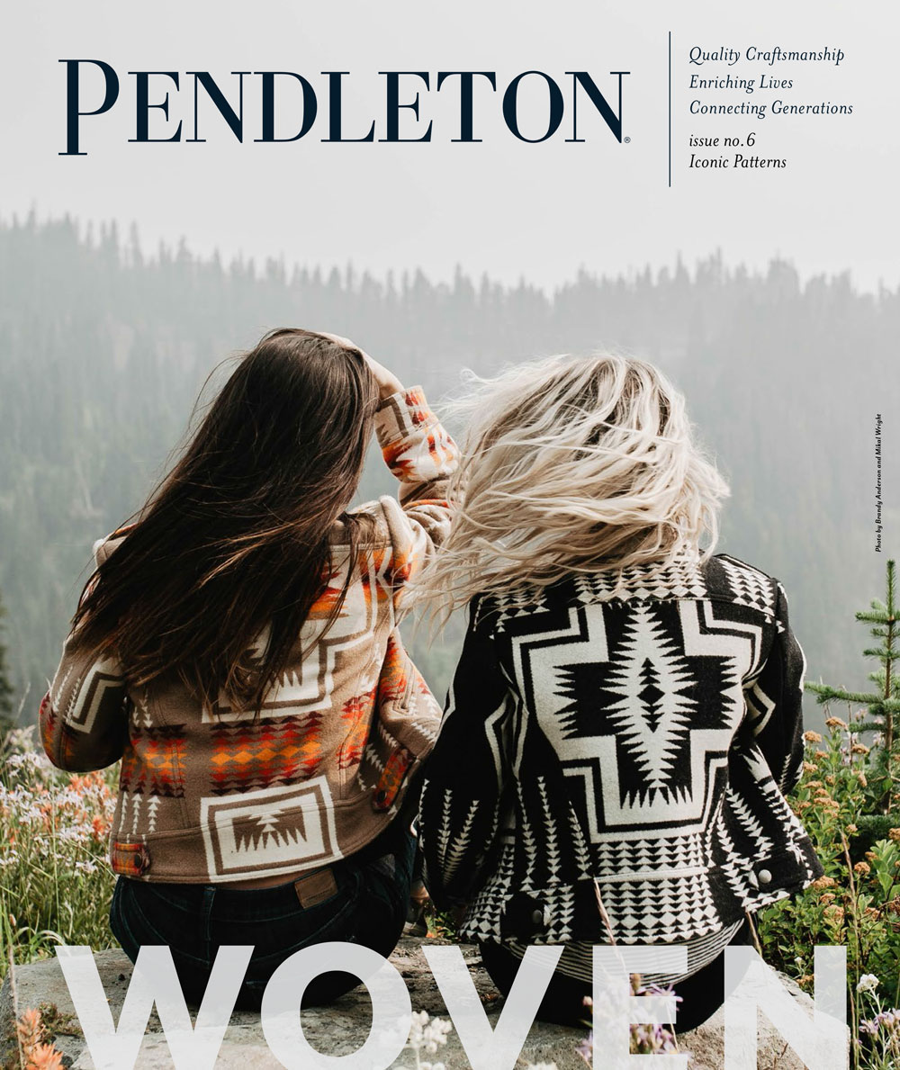 two women with long hair sit on a hilltop wearing Pendleton jackets