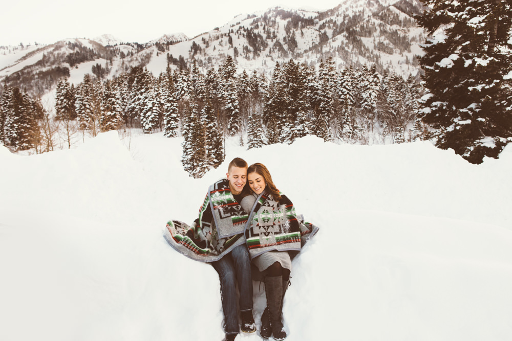 A couple in the snow, wrapped in a blanket