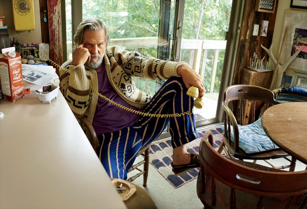 Jeff Bridges relaxes in his kitchen, wearing pajama pants, purple T-shirt, moccasins and his Westerley sweater and holding a phone receiver in his hand.