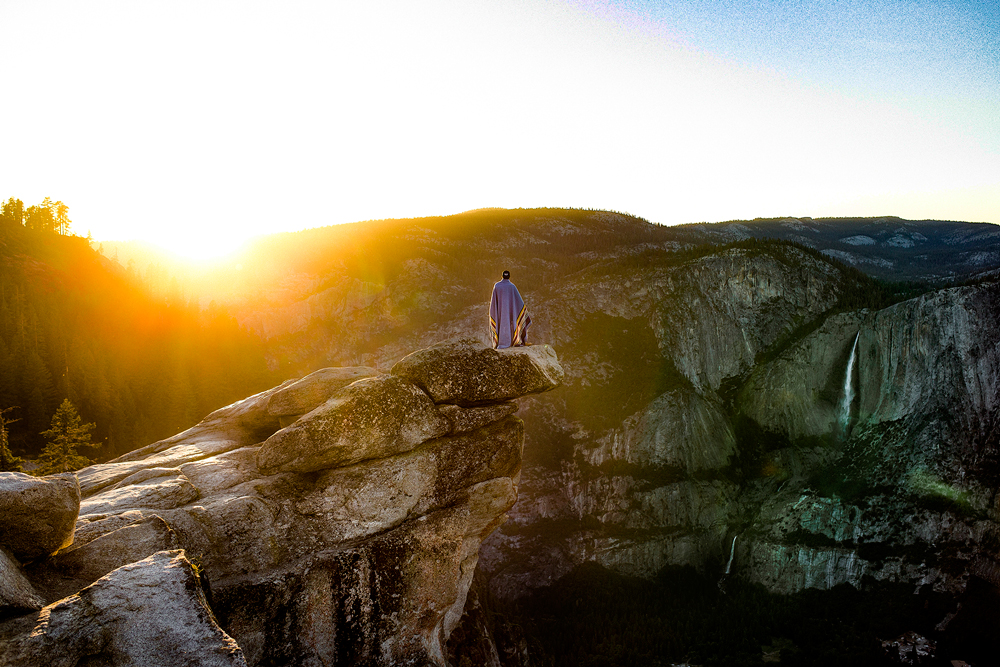 A woman wrapped in a blanket stands looking at the Yosemite landscape - photo by Allie Taylor