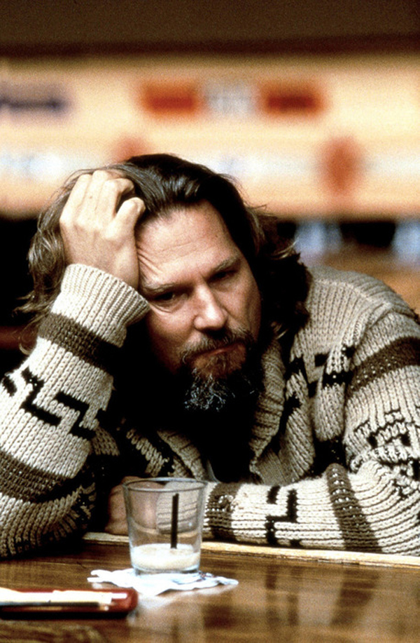 Jeff Bridges as Jeff Lebowski, AKA "The Dude," sits at the bolwing alley bar with a white Russian in front of him.