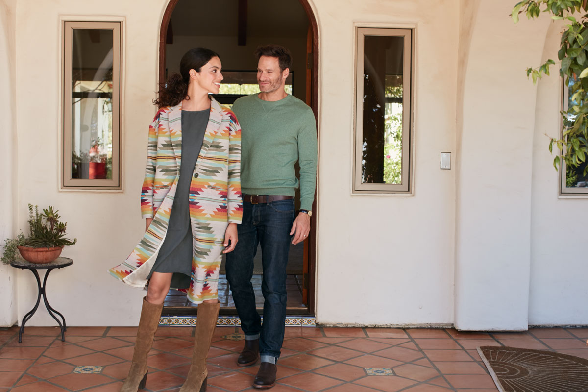 A man and woman stand by a doorway, and she is wearing a coat in the Falcon Cove pattern