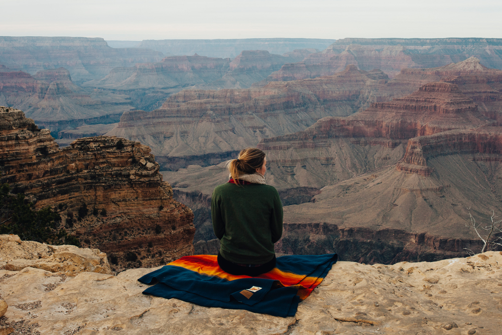 woman with ponytail seated on a Pendleton Grand Canyon park blanket overlooking the rim of the Grand Canyon