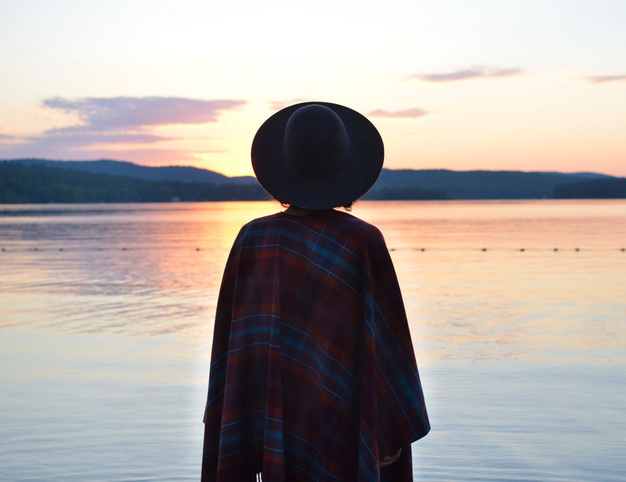 A woman stands by the sore of the lake at sunrise, wrapped in a plaid Pendleton throw.