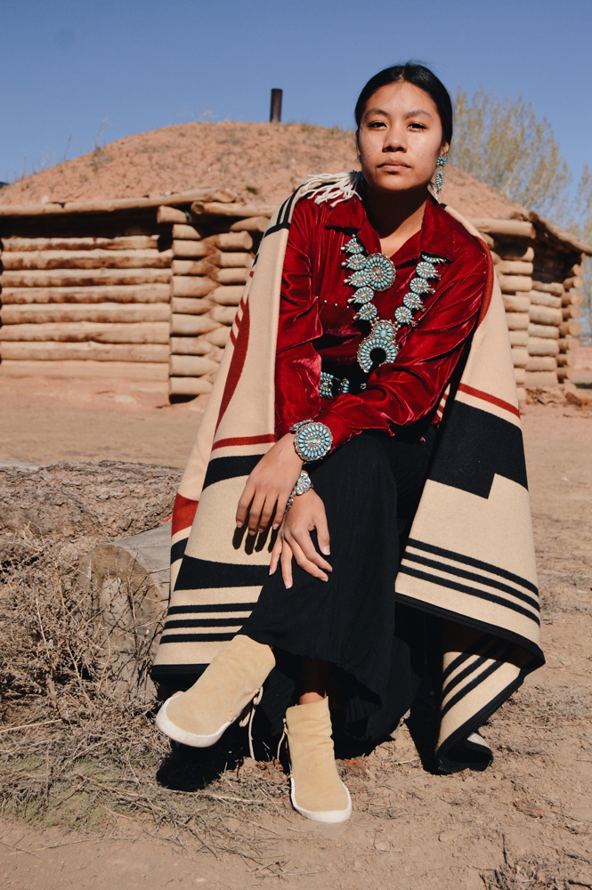 Shondina Lee Yikasbaa poses in traditional Dine clothing, family jewelry, and the Gift of the Earth blanket. 