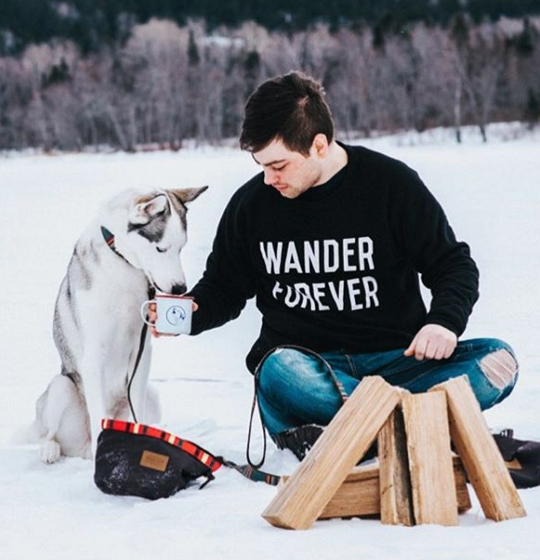 A young man gives his husky a drink from a tin coffee cup. 