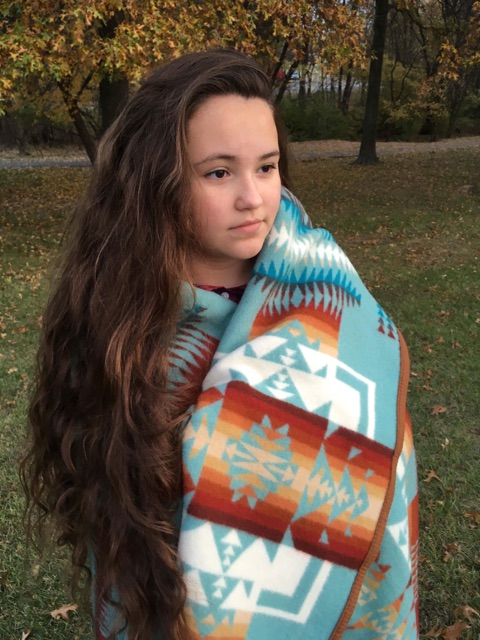 A young Native American woman with very long hair stands in a meadow