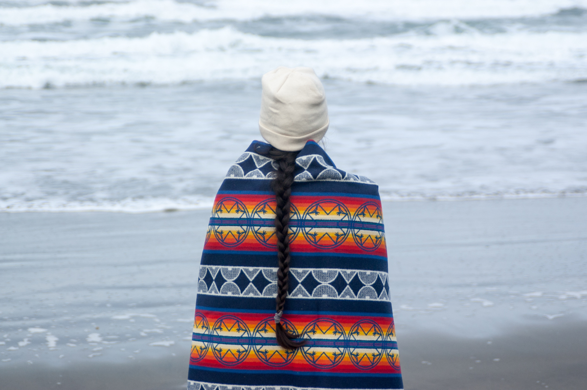 A woman shows off the We Walk Together blanket at Fort Stevens beach.