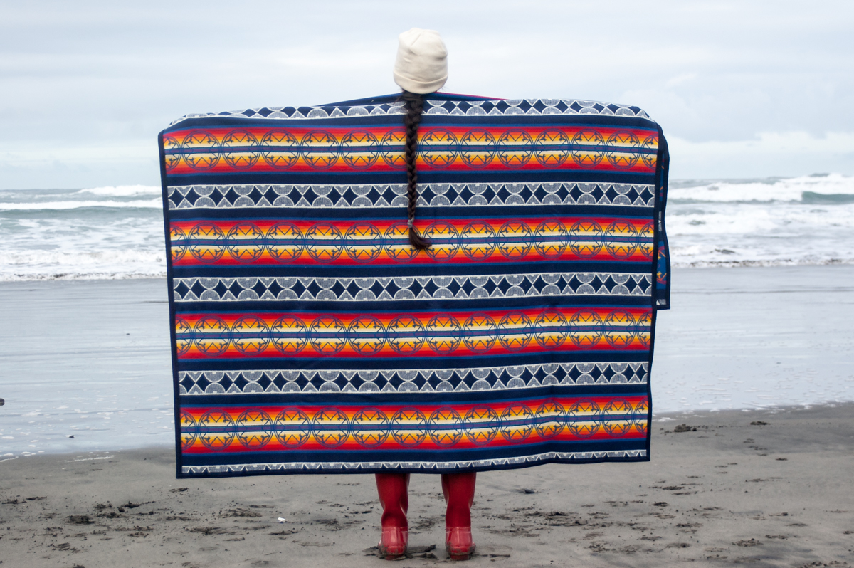 A woman shows off the We Walk Together blanket at Fort Stevens beach.