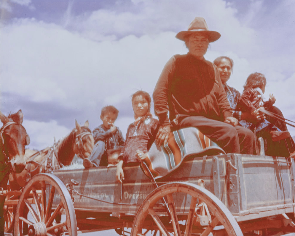 Archival photo from early 1900s of a Navajo family (father, mother, three young children) riding in a wagon with a Pendleton serape stripe blanket