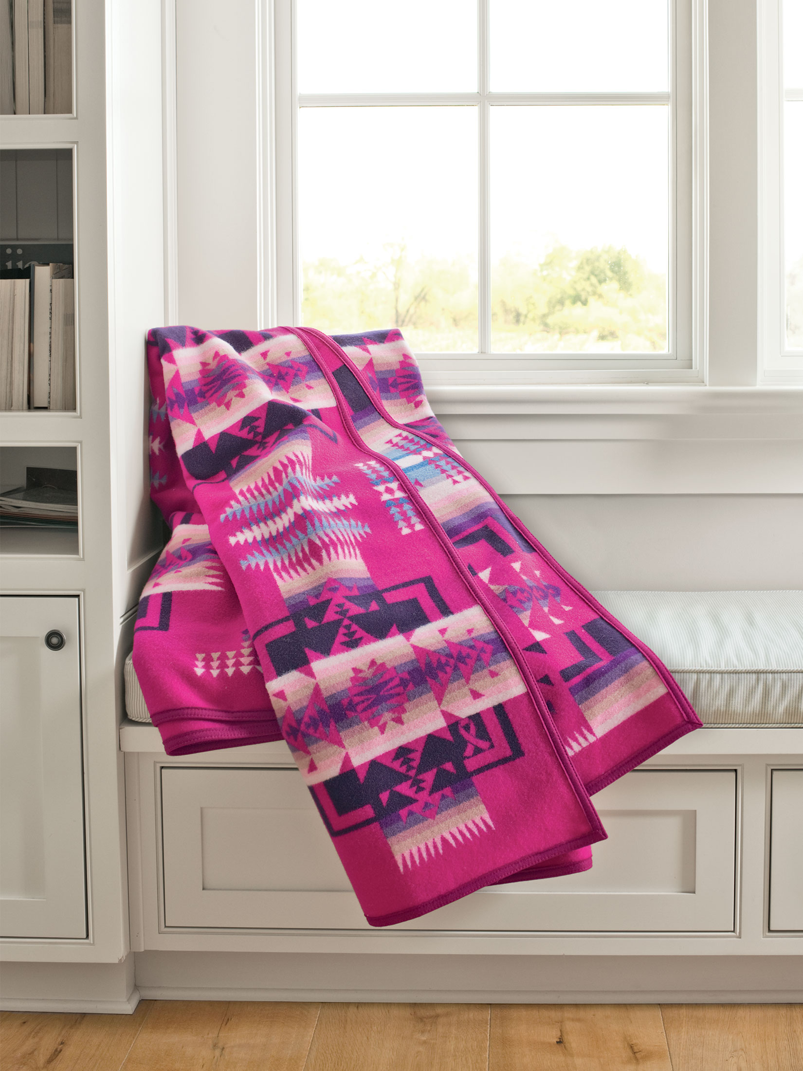 A cherry-pink Chief Joseph blanket, folded and draped on a windowseat. This special blanket benefits the Native American women's clinic at NARA.