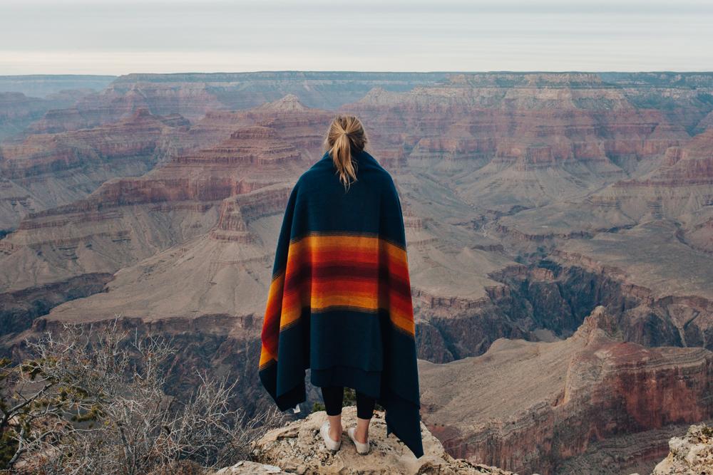 woman with ponytail wrapped in Pendleton Grand Canyon blanket stands on the rim of the Grand Canyon