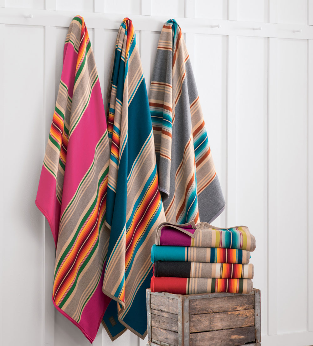 Pendleton serape stripe blankets hanging on pegs, next to a stack of folded Pendleton serape stripe blankets