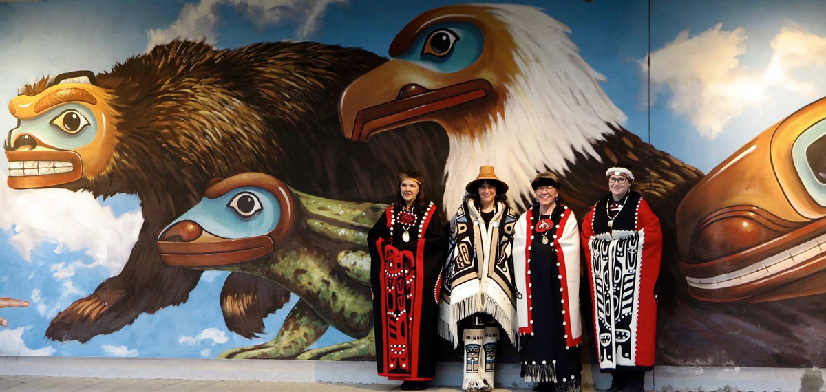 Linda and family in their handmade blankets in front of a mural