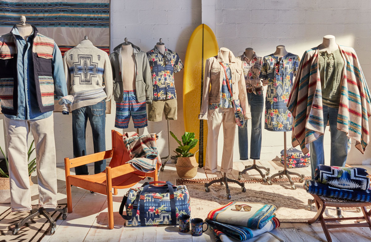 A photo of the goods included in the Pendleton collaboration with Tommy Bahama, including a vest, a sweater, a hoodie, a shirt, a bag, a poncho and a blanket. These goods are displayed on dressmaker forms in a sunny room.