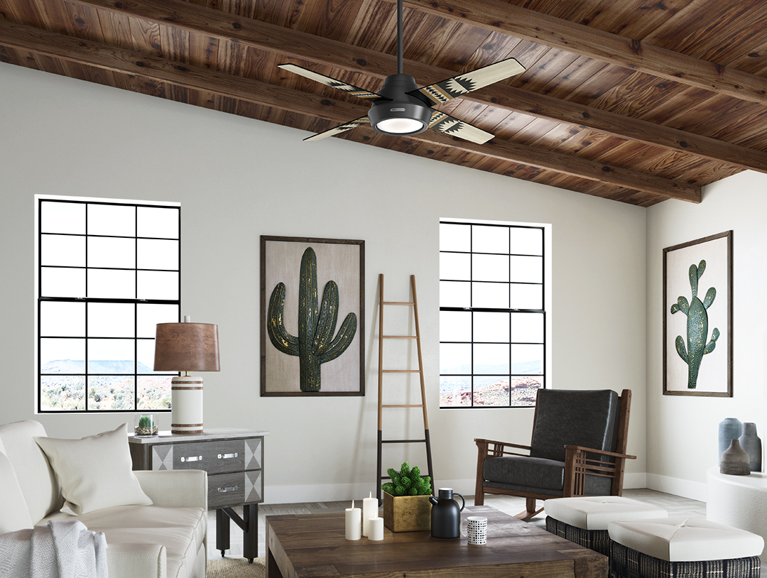 A living room featuring the Pendleton x Hunter fan. the room has white walls and a vaulted ceiling that's covered in wood, and paintings of cacti on the walls.