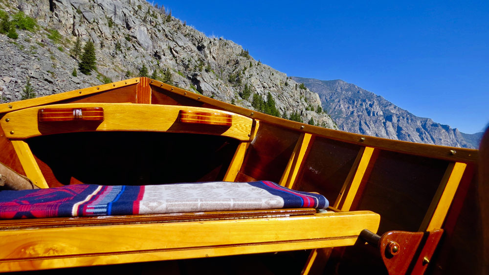 Photo taken inside a handmade wooden drift boat, showing the Pendleton Bighorn blanket on the boat's seat, against a backdrop of Montana mountains.