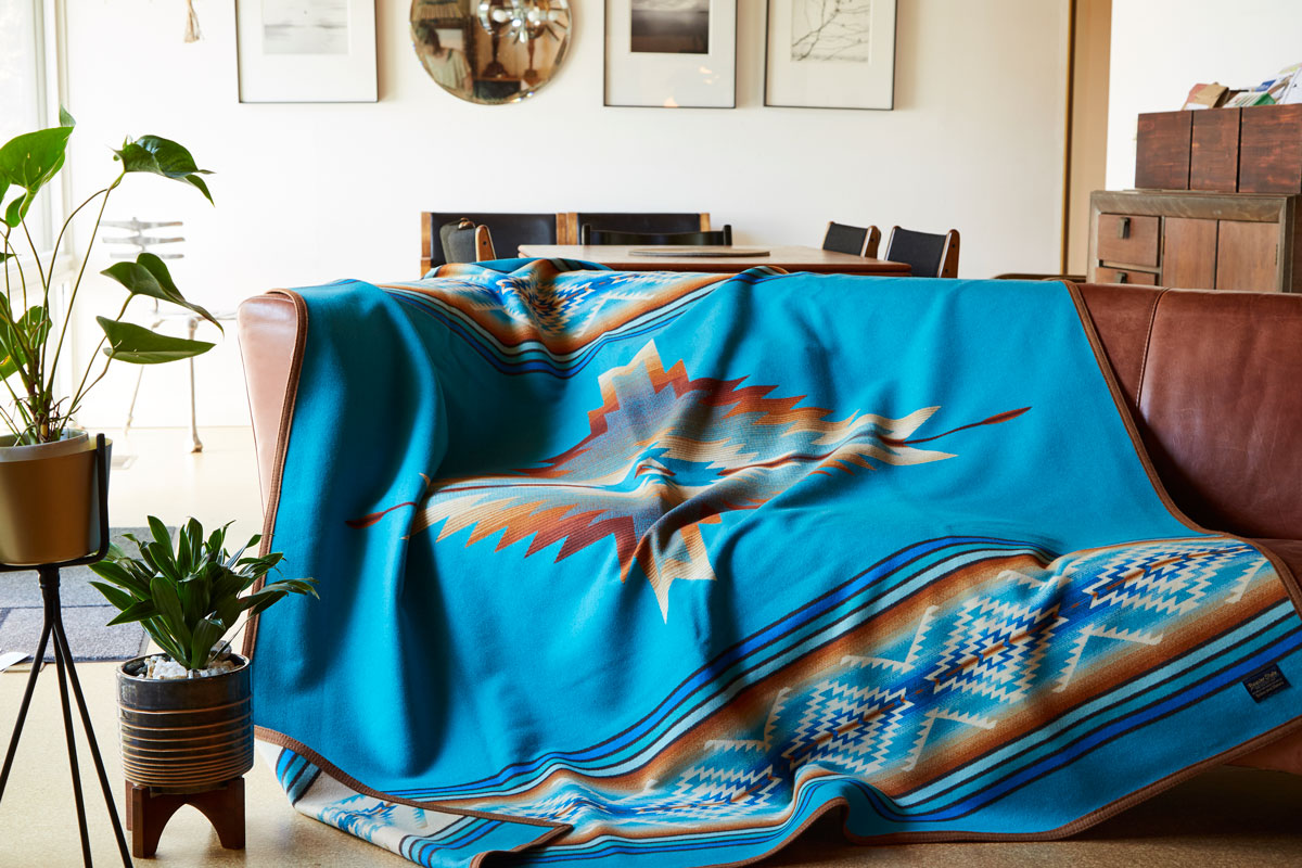 A very stylish living room, with a Pendleton Pagosa Springs blanket draped over a brown leather sofa.