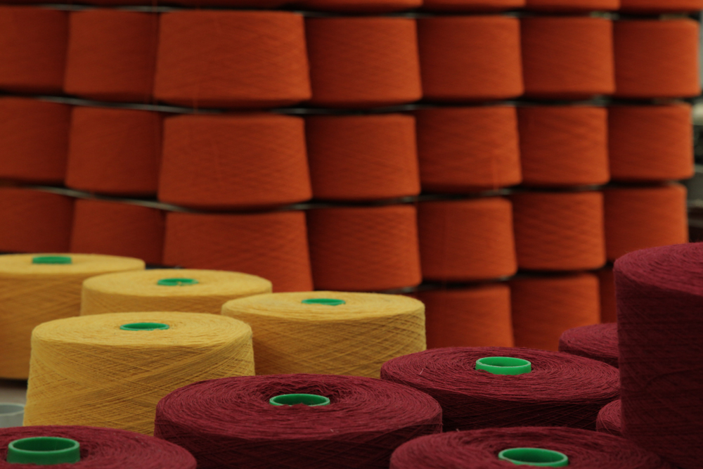 brightly colored spools of spun wool wait to be threaded onto a loom