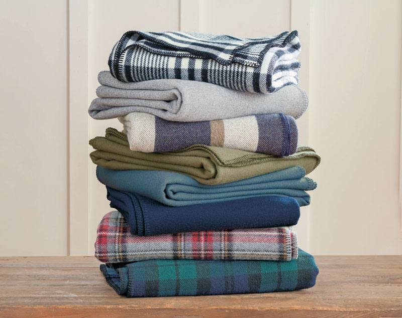 Another stack of folded Pendleton Eco-Wise Wool bed blankets on a wooden table.