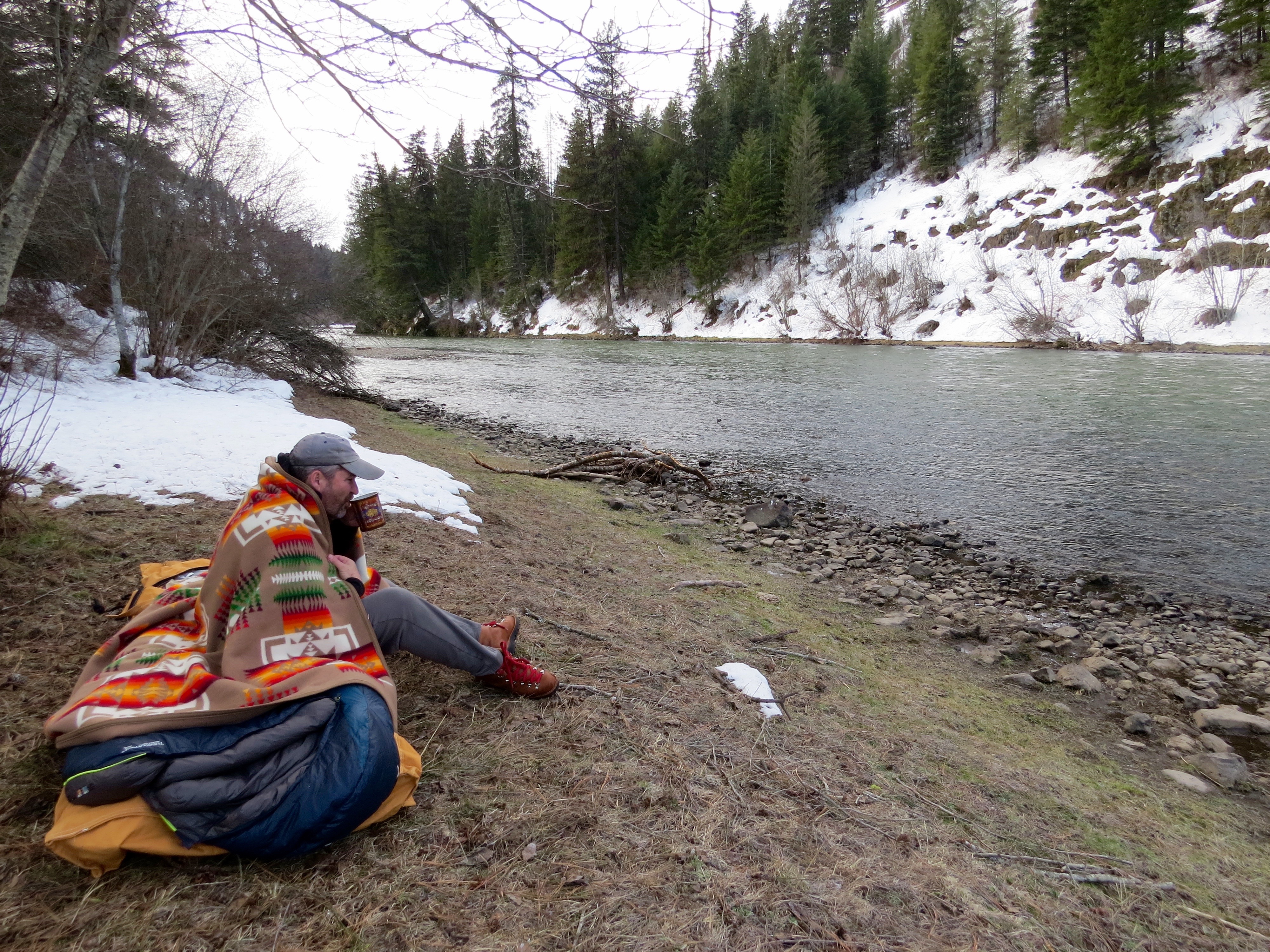 Greg Hatten sits on the banks of the Wallowa River, sipping a warm drink. 