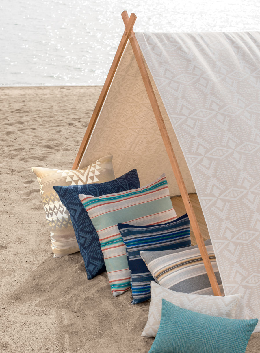 A sandy beach and a tent made of Pendleton by Sunbrella outdoor fabrics, holding a group of throw pillows.