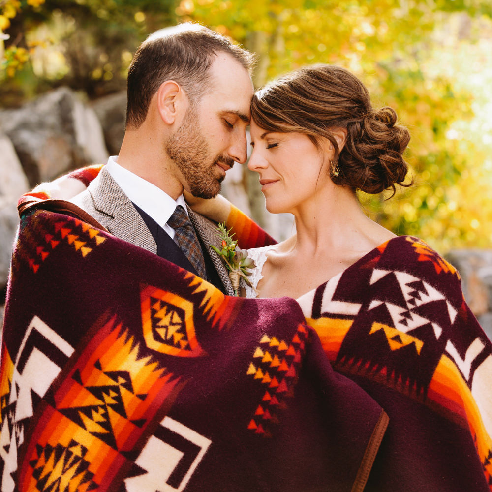 A couple embraces in their wedding attire, wrapped in a Pendleton Chief Joseph blanket