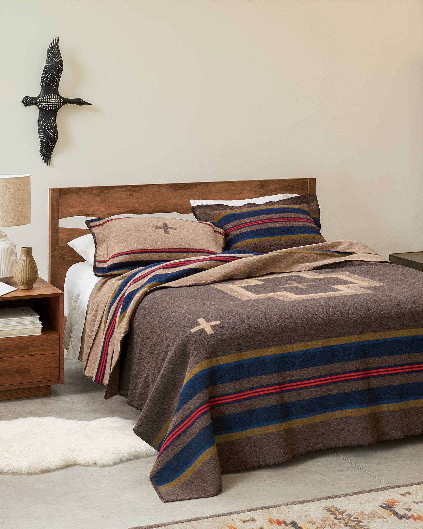 Bed with Shelter bay Pendleton blanket. Blanket is brown with navy, tan and red stripes, and large tan central cross, with smaller crossed in corners.