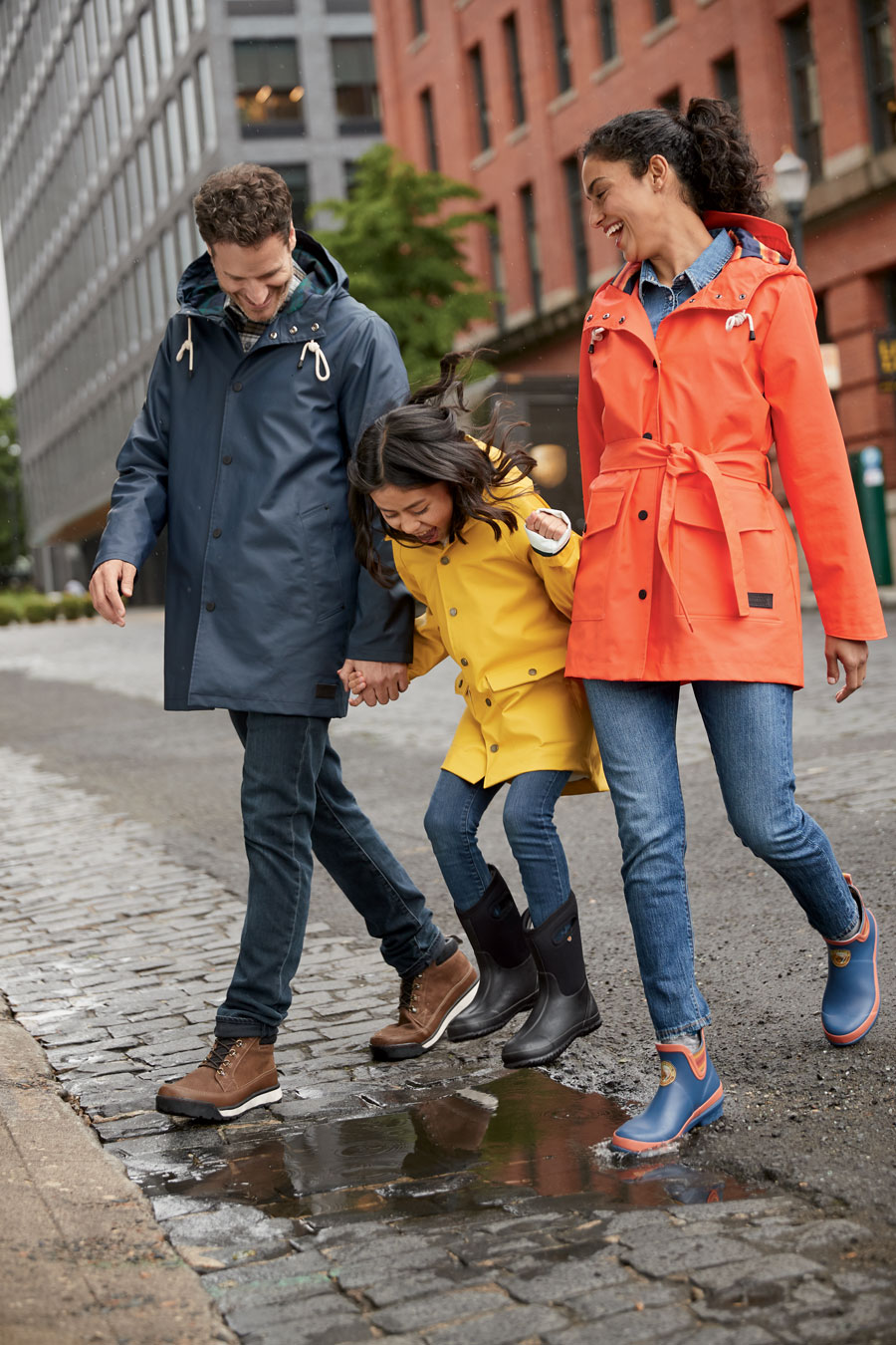 A man, a child, and a woman crossing a cobblestone street wearing Pendleton rain coats.