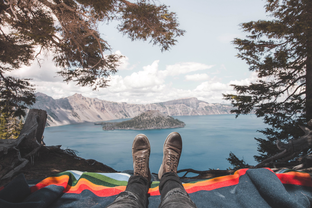 Kyle Houck - a pair of booted feet on a Crater Lake blanket, with the lake ahead.