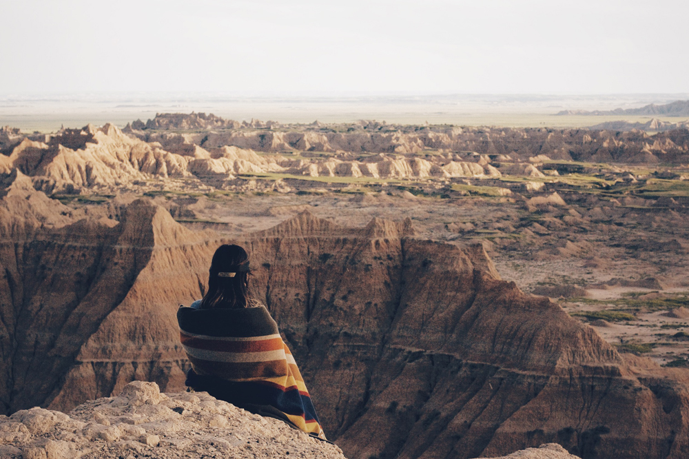 Woman wrapped in blanket looks out into a crevasse in the Badlands