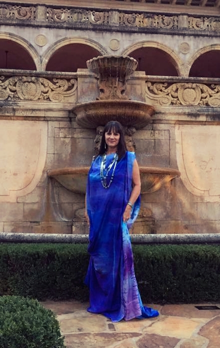 Artist Wendy Ponca poses before a stone fountain in one of her own flowing creations, a gown in shades of royal blue and purple.