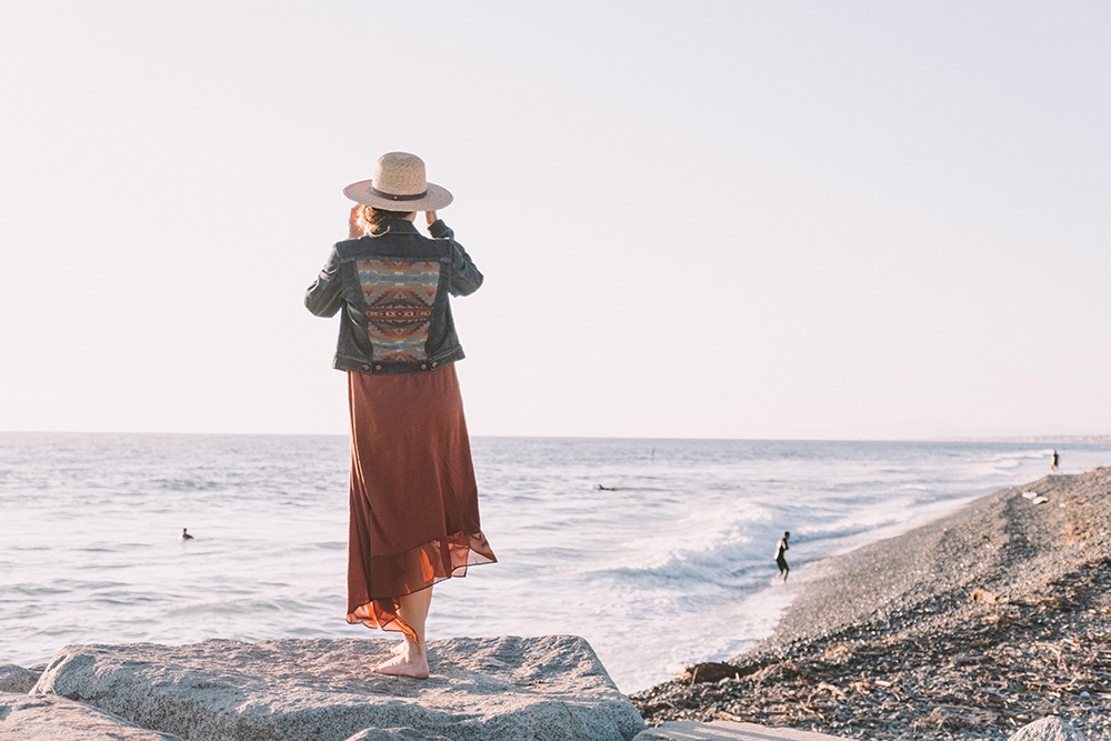 A woman stands on the beach, looking out to sea.