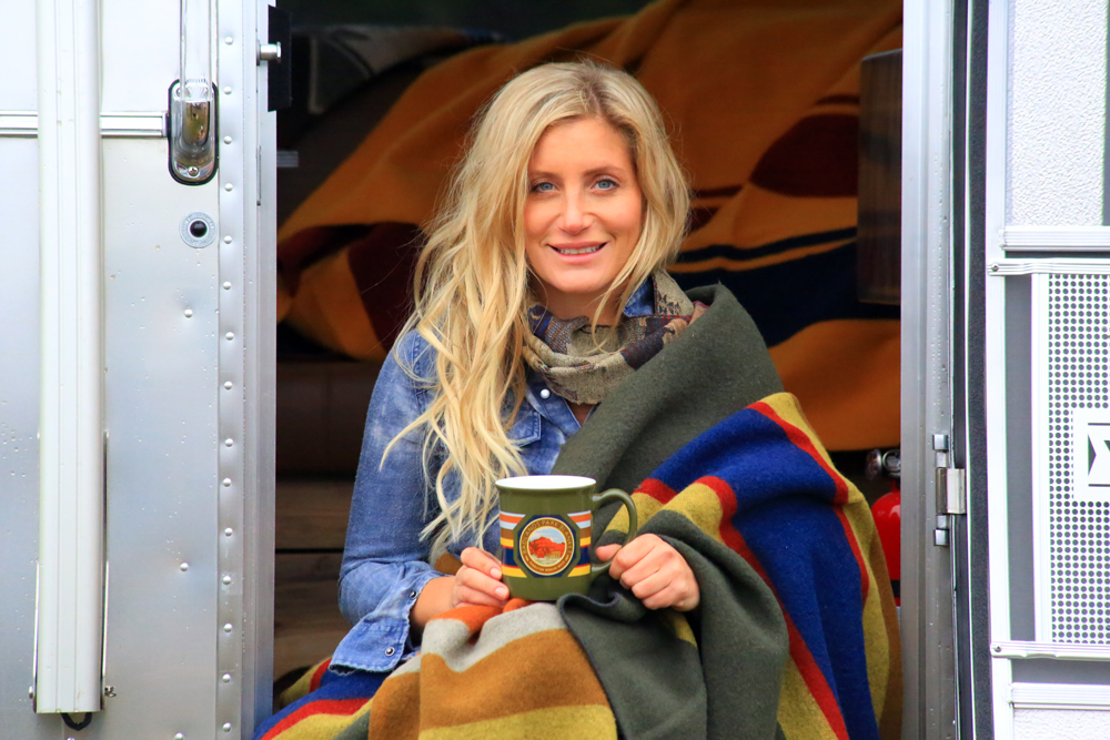 a woman wrapped in a Pendleton blanket sits on the entry steps of the Pendleton Airstream