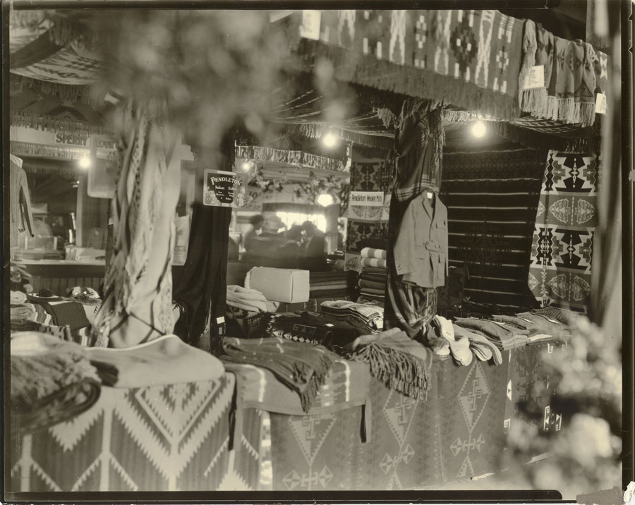 Circa 1911 –A cozy counter display of Pendleton blankets, steamer rugs (fringed throws), wool socks and men’s hunting jacket.