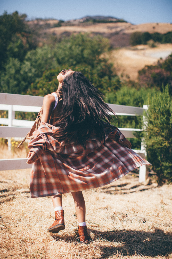 A young woman with long dark hair wears a brown and white plaid pendleton shirt