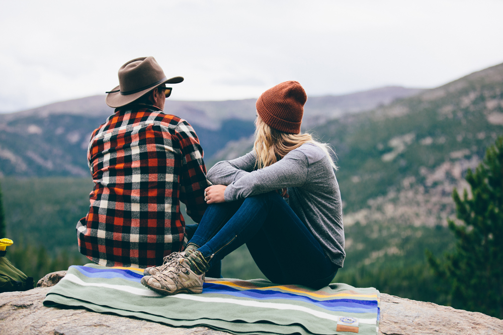 Kate Rolston photo of a man and woman earing hats, sitting on a rocky outcrop on a Pendleton blanket. 