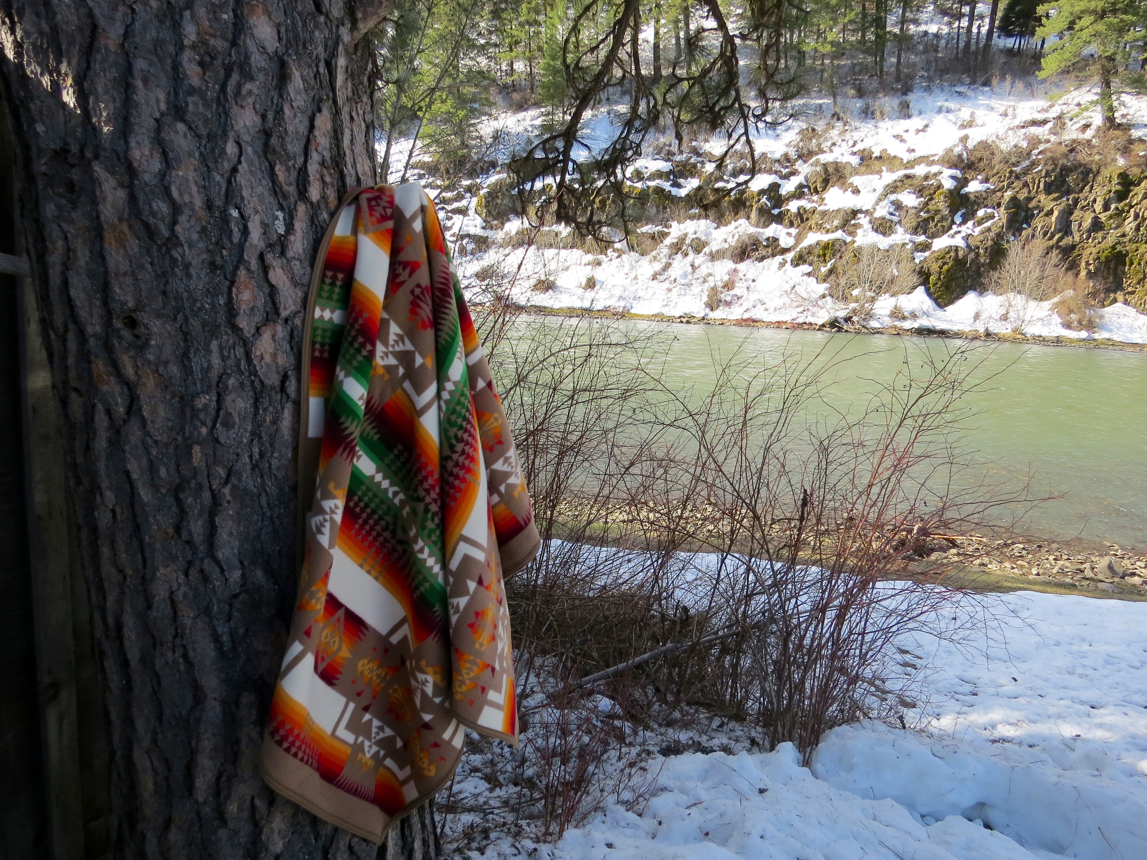 A Chief Joseph blanket hangs on a tree by a riverbank. 