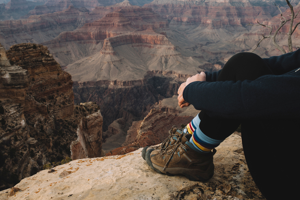 seated woman at rim of Grand Canyon, wearing hiking boots and Pendleton socks.