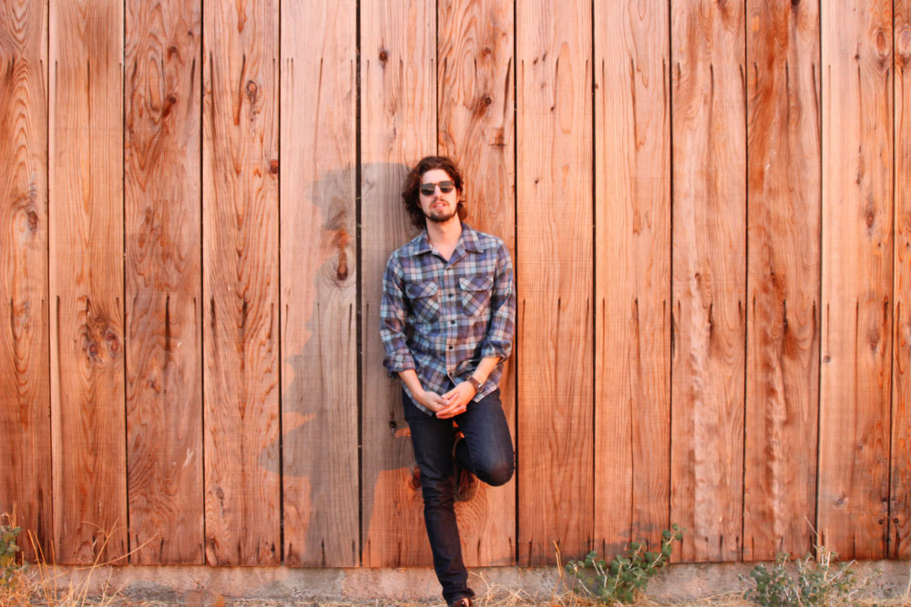 Musician Ben Jaffe leans against a cedarwood wall. He is wearing a Pendleton Board Shirt in Original Surf Plaid.