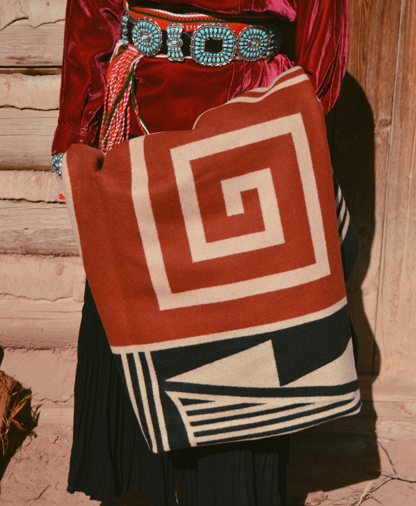 Shondina Lee Yikasbaa poses in traditional Dine clothing, family jewelry, and the Gift of the Earth blanket. 