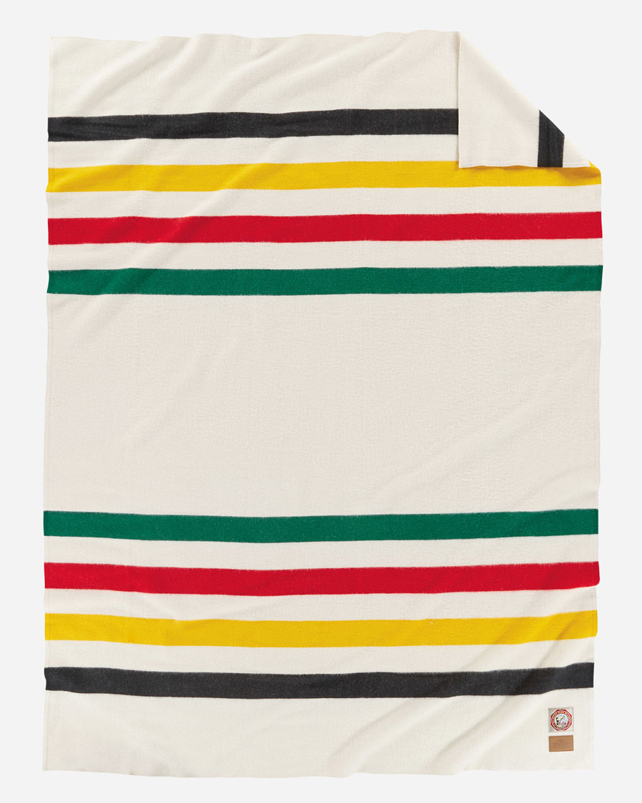 The Glacier National Park blanket, by Pendleton. A white background with a stripe of black, yellow, red and green at each end.